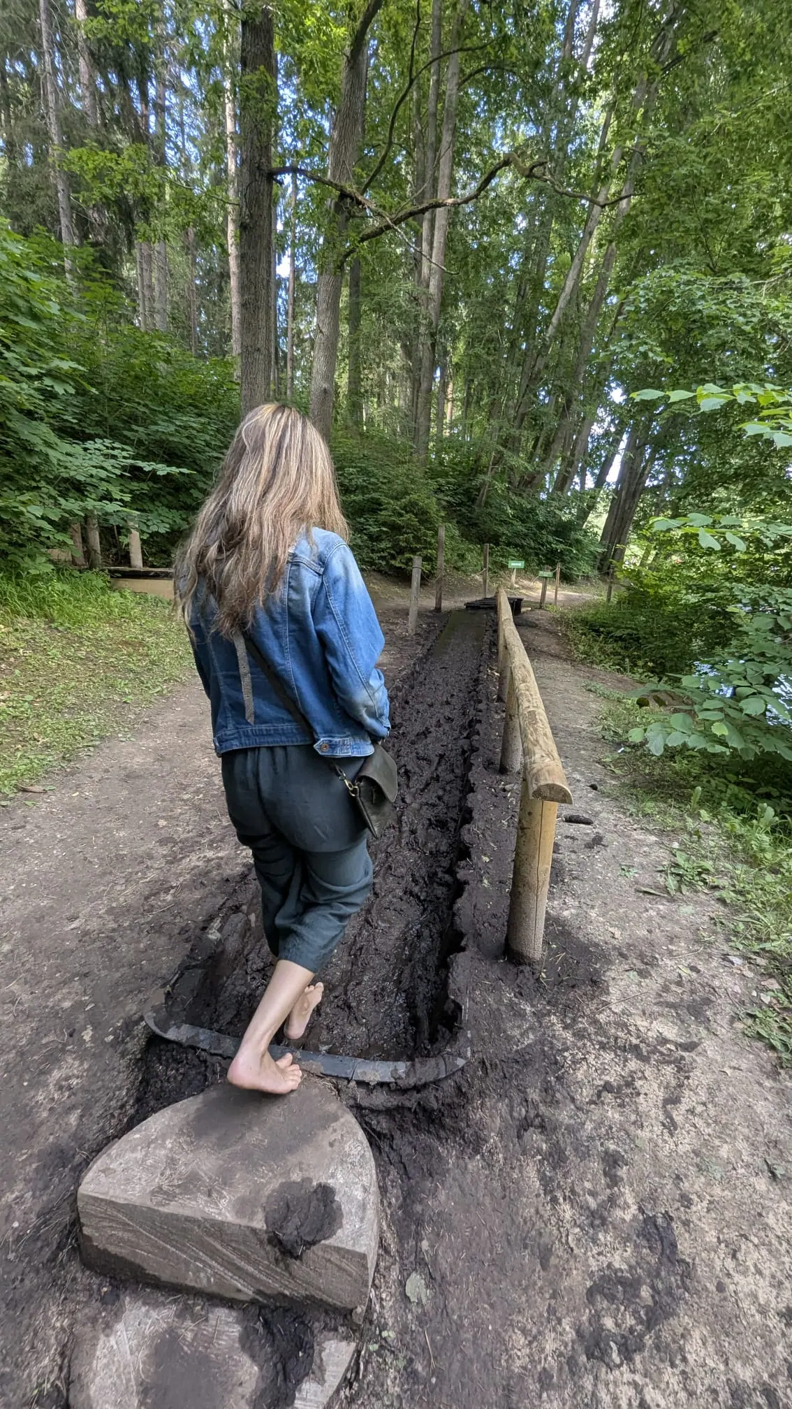 A visitor walking barefoot through a muddy section of the trail