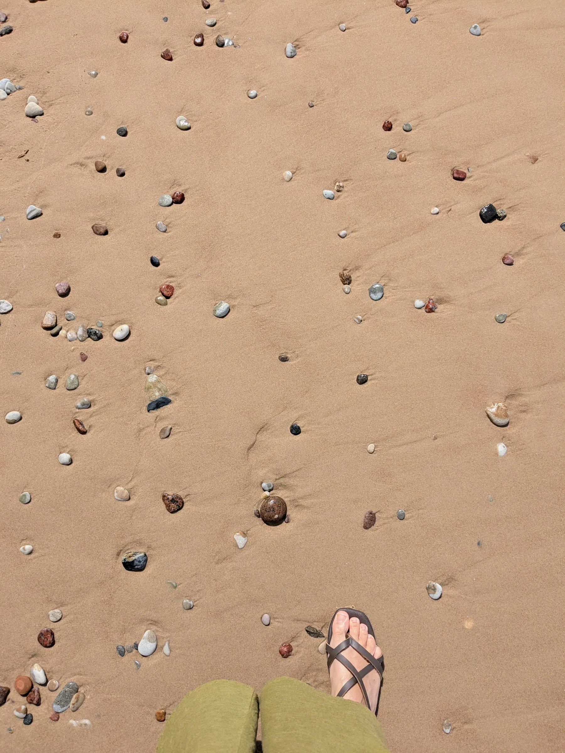 Small multicoloured stones scattered across the sand on Pāvilosta beach