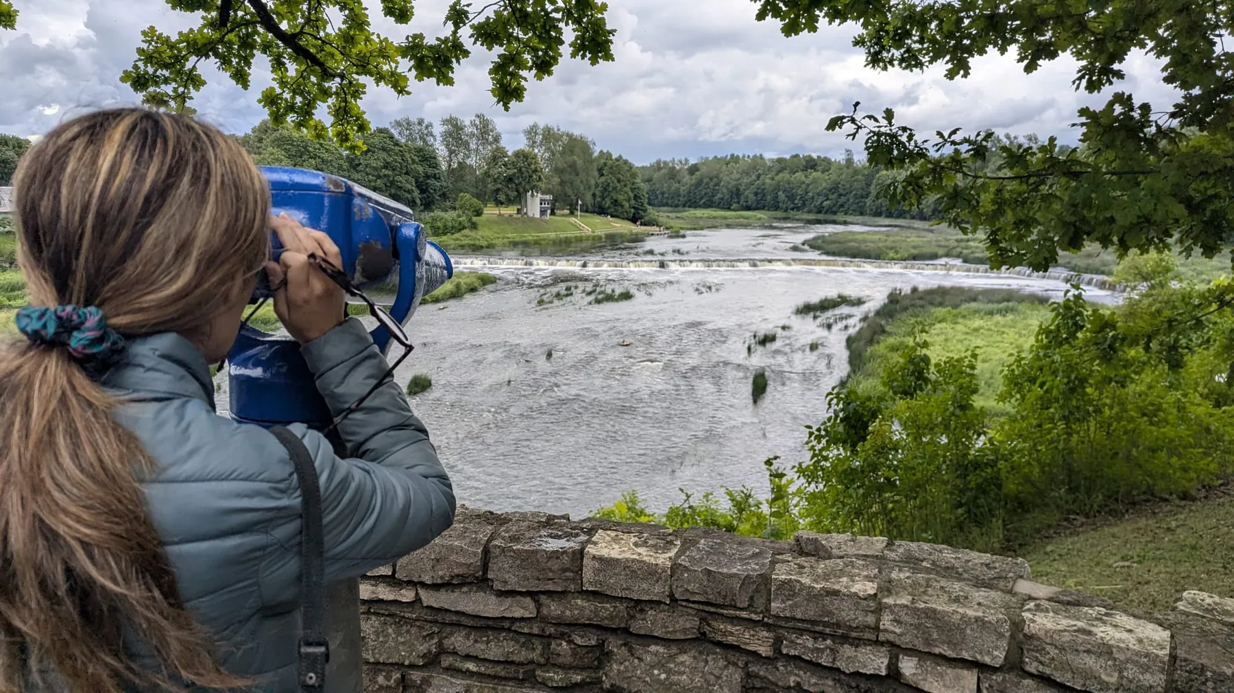 A visitor using the free binocular beside Ventas Rumba in Kuldīga