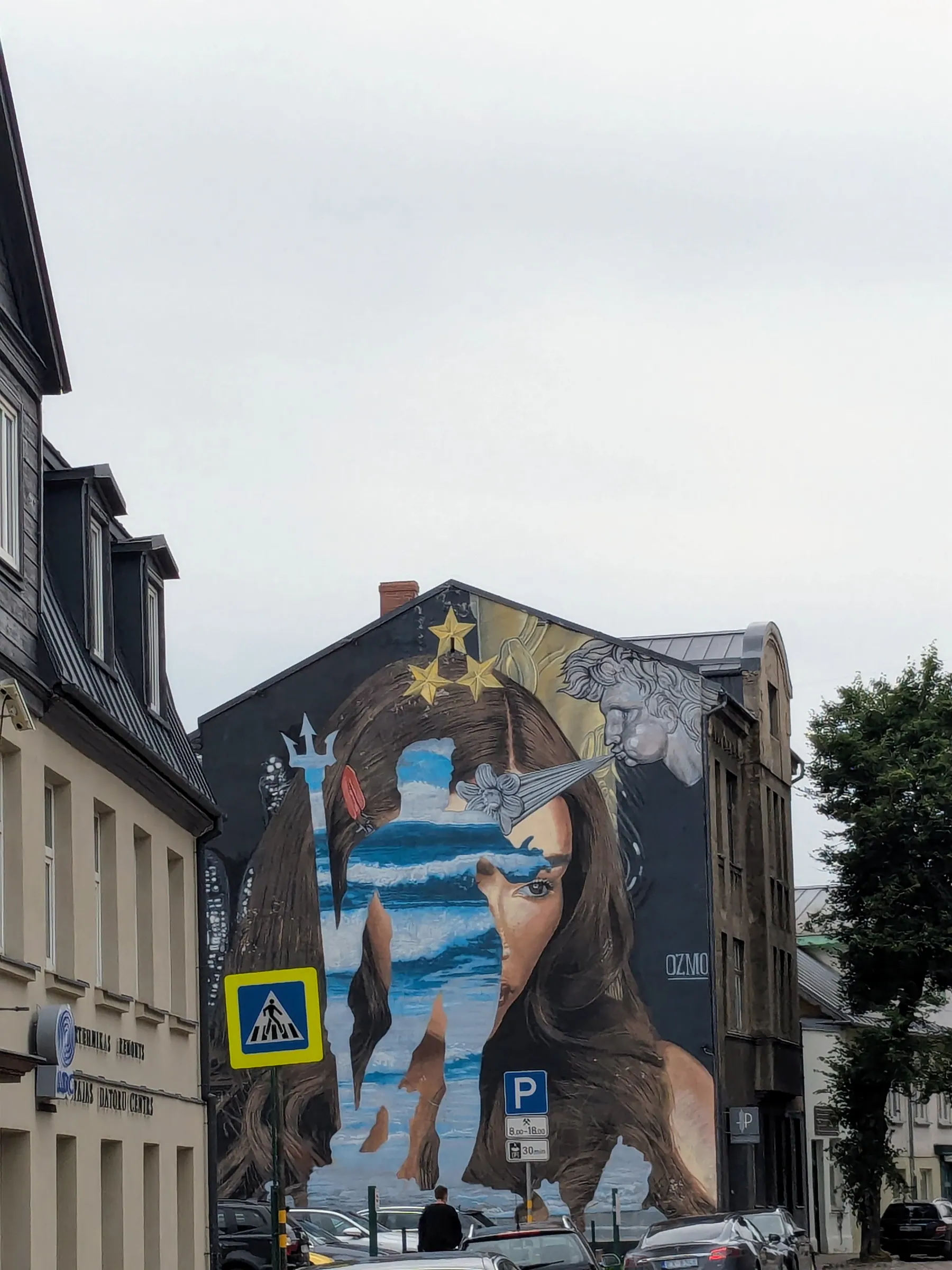 A towering blue-toned mural above a Liepāja side street