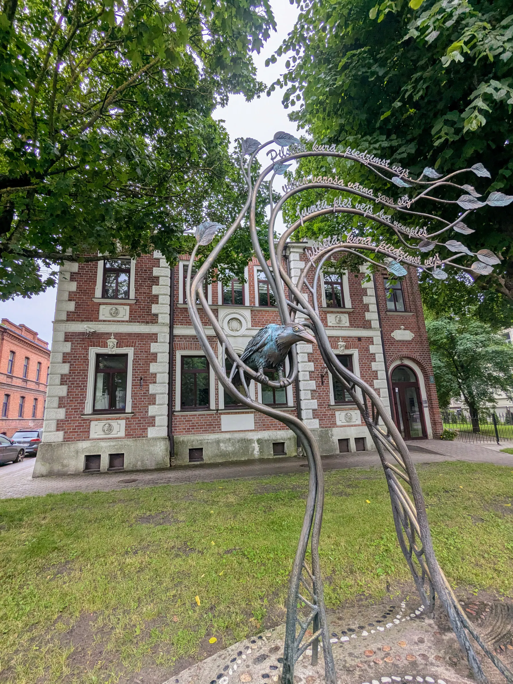 A metal character sculpture from Liepāja's anthem among the trees