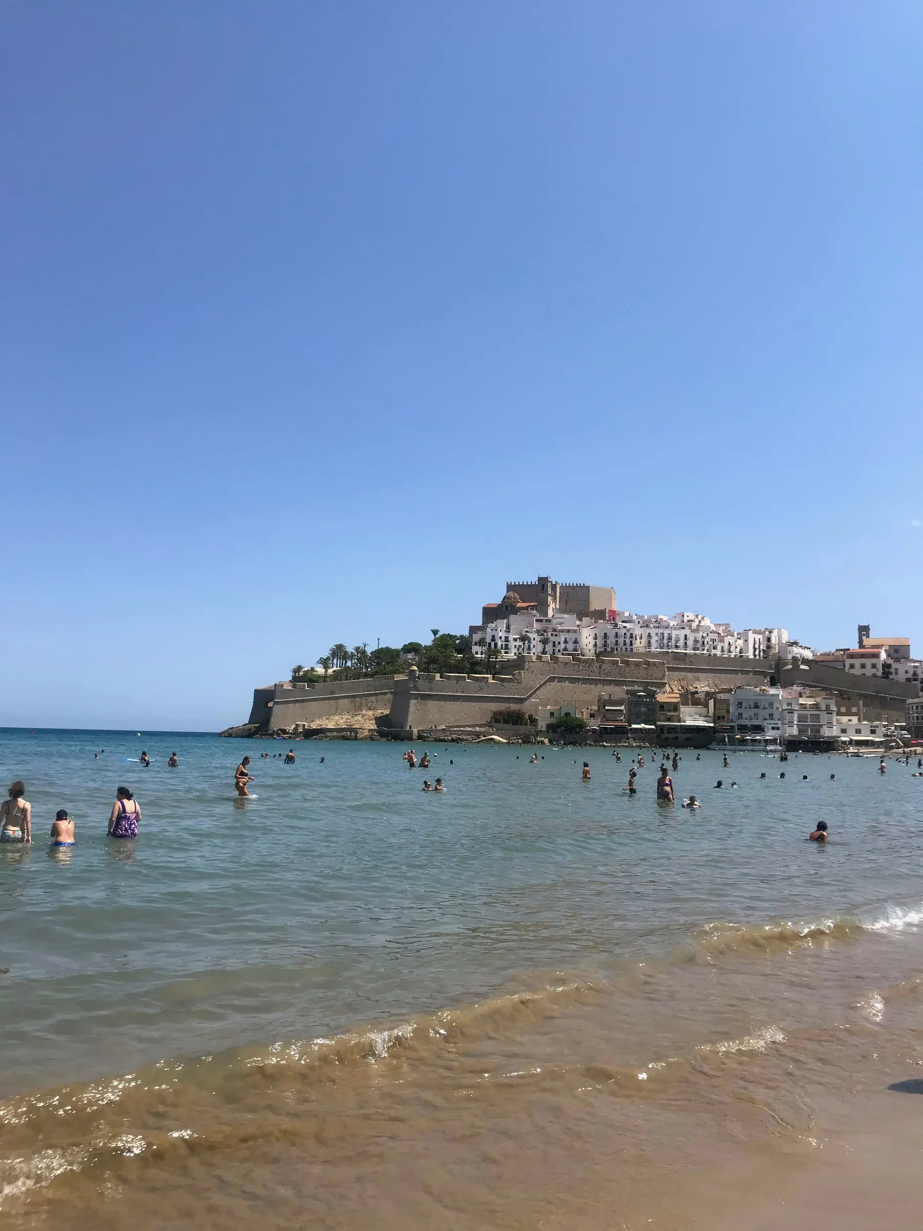 People swimming at sandy Playa Norte with Peñíscola Castle behind them